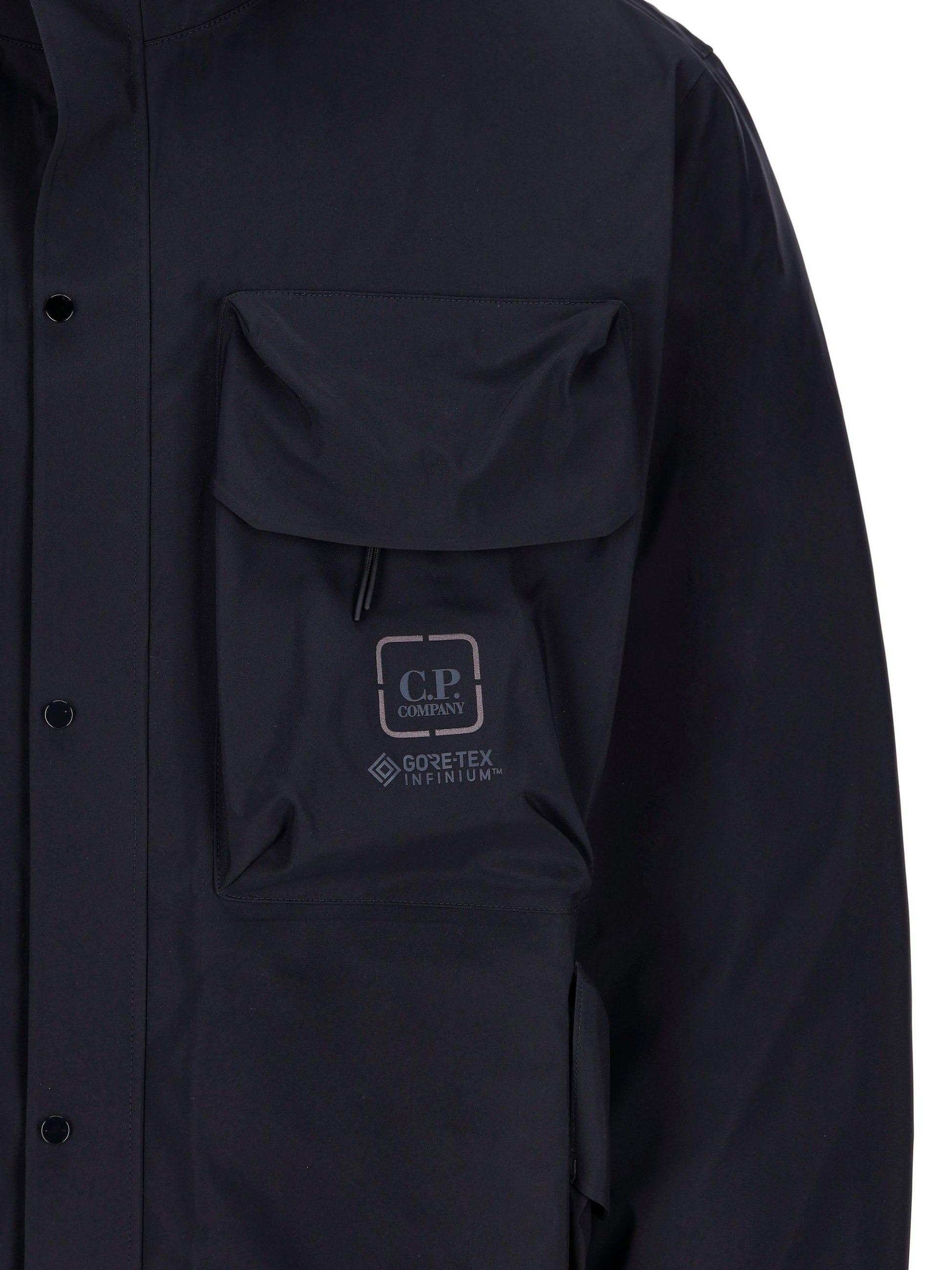 Giacca realizzata in poliammide di colore blu scuro, con maxi tasche sul petto con logo. 15CLOW007A 005967A888 C.P COMPANY 